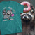 A Tshirt with a raccoon running wild carrying a donut. The words live, laugh, loot surround the raccoon. 
In the background behind the tshirt, a raccoon holds aloft a pink glazed donut with sprinkles. 
